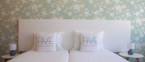 A double bed with two pillows, a nightstand, a lamp, and a floral wallpaper.