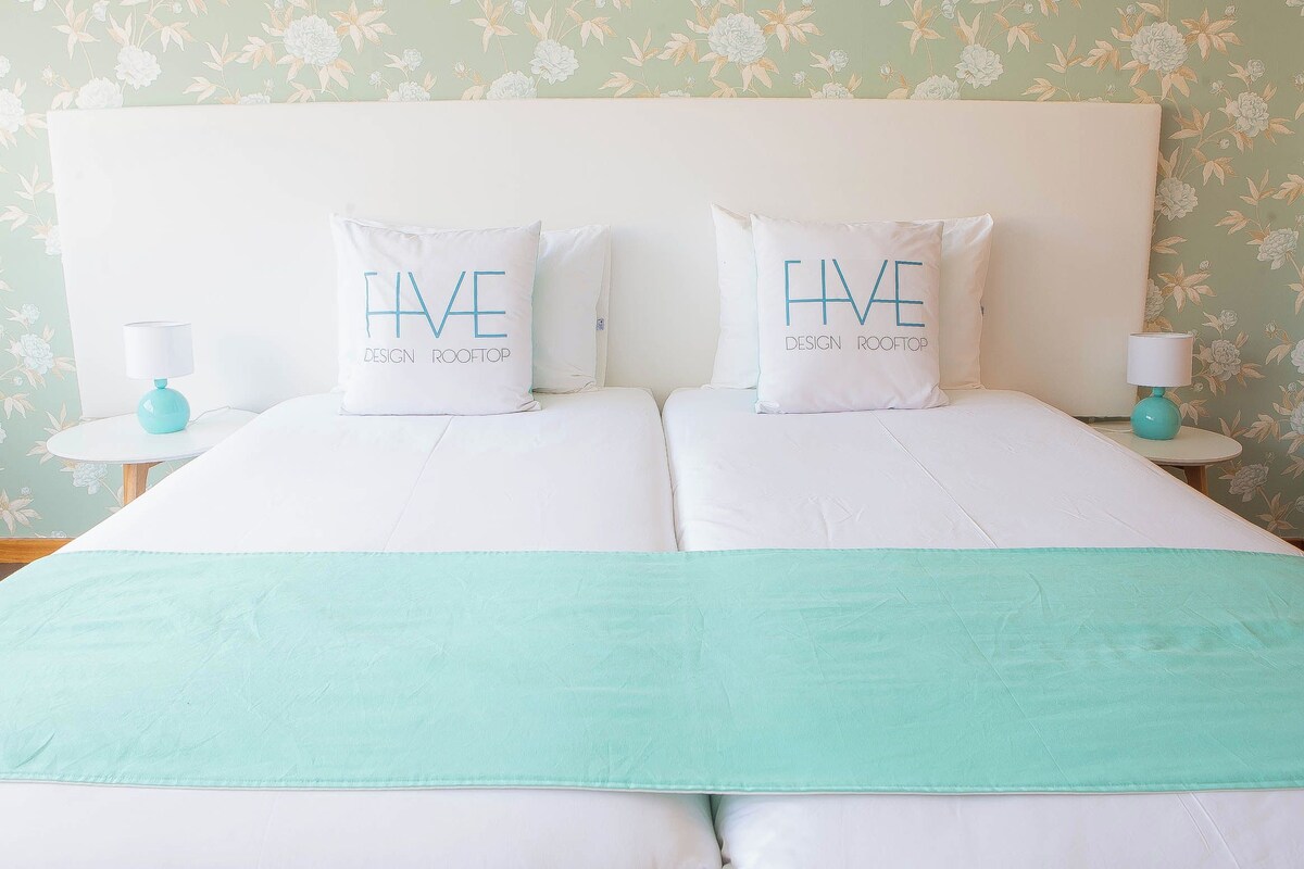 A double bed with two pillows, a teal throw blanket, and matching teal lamps on side tables.
