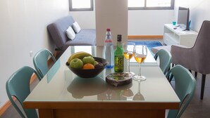 A dining area with a glass table, teal chairs, a bowl of fruit, and bottles of liquor. - Five Design Rooftop by Storytellers (Funchal)