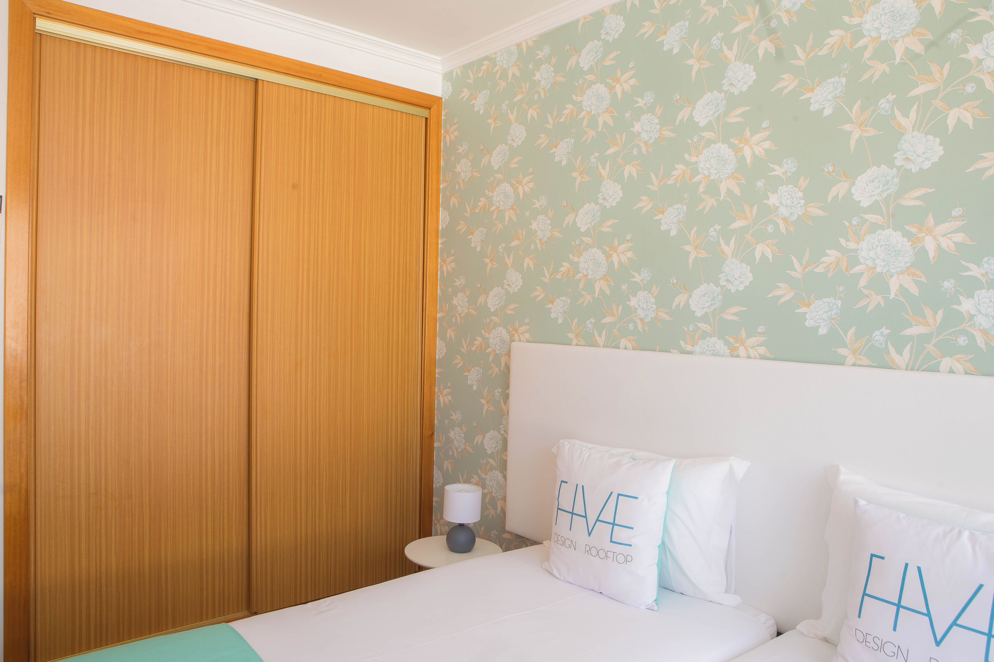 A bedroom with a bed, pillows, a nightstand, and a wooden wardrobe.