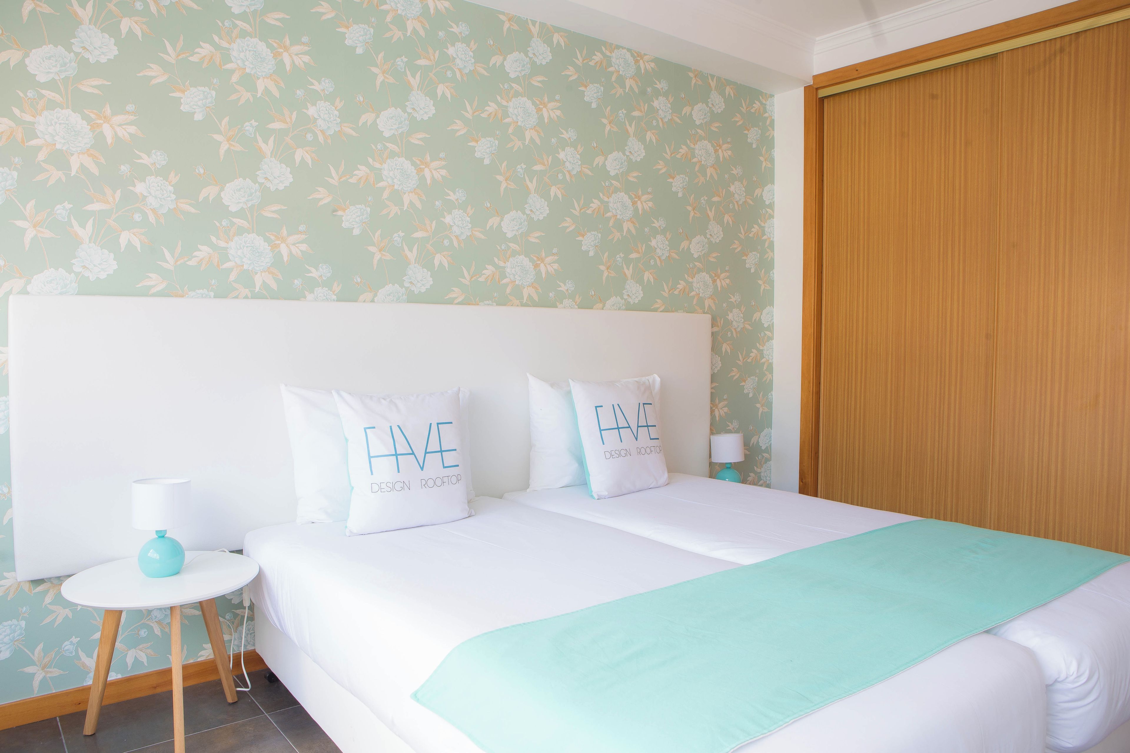 A hotel room with a bed, two pillows, a bedside table, a lamp, and a wooden wardrobe.