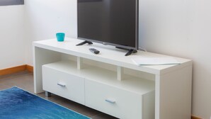 A white TV stand with a flat-screen TV, a remote control, and a glass on top. - Five Design Rooftop by Storytellers (Funchal)