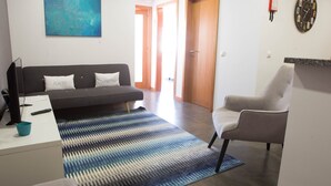 A modern living room with a grey sofa, a blue and white striped rug, a grey armchair, a flat-screen TV, and a small table with a remote control and a blue cup. - Five Design Rooftop by Storytellers (Funchal)