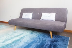 En grå sofa med to hvide puder, hvoraf den ene har teksten 'PURE' og den anden 'FEELING', placeret på en blød blå og hvid stribe-rug.