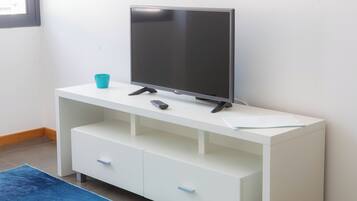 A white TV stand with a flat-screen TV, a remote control, and a teal cup.
