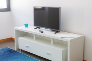 A white TV stand with a flat-screen TV, a remote control, and a teal cup. - Five Design Rooftop by Storytellers (Funchal)