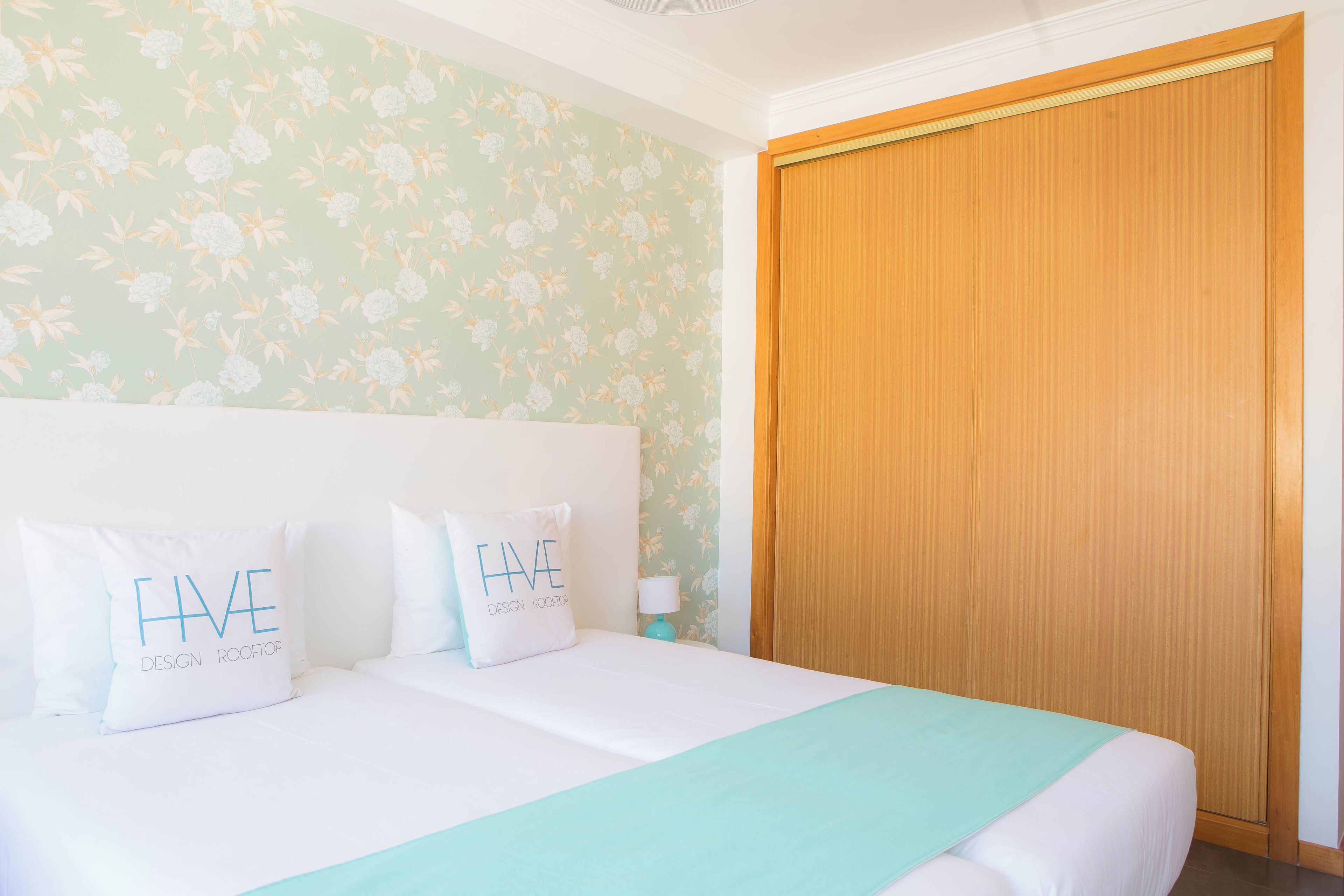 Habitación de hotel con una cama, dos almohadas, una mesita de noche, una lámpara y un armario de madera.