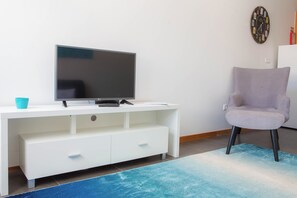 En moderne stue med et fladskærms-tv på et hvidt tv-møbel, en grå lænestol og en blå måtte.