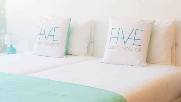 A hotel room with two beds, each with a pillow that reads 'HAVE DESIGN ROOFTOP'.