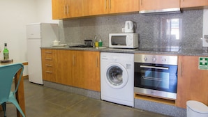 A compact kitchen with wooden cabinets, a washing machine, a microwave, and a small refrigerator.