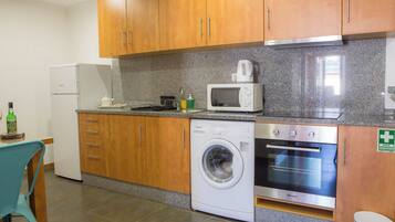 A compact kitchen with wooden cabinets, a washing machine, a microwave, and a small refrigerator.
