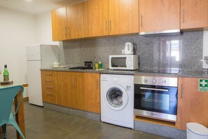 A compact kitchen with wooden cabinets, a washing machine, a microwave, and an oven. - Five Design Rooftop by Storytellers (Funchal)