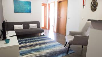 A modern living room with a sofa, a chair, a rug, a painting, and a clock on the wall.