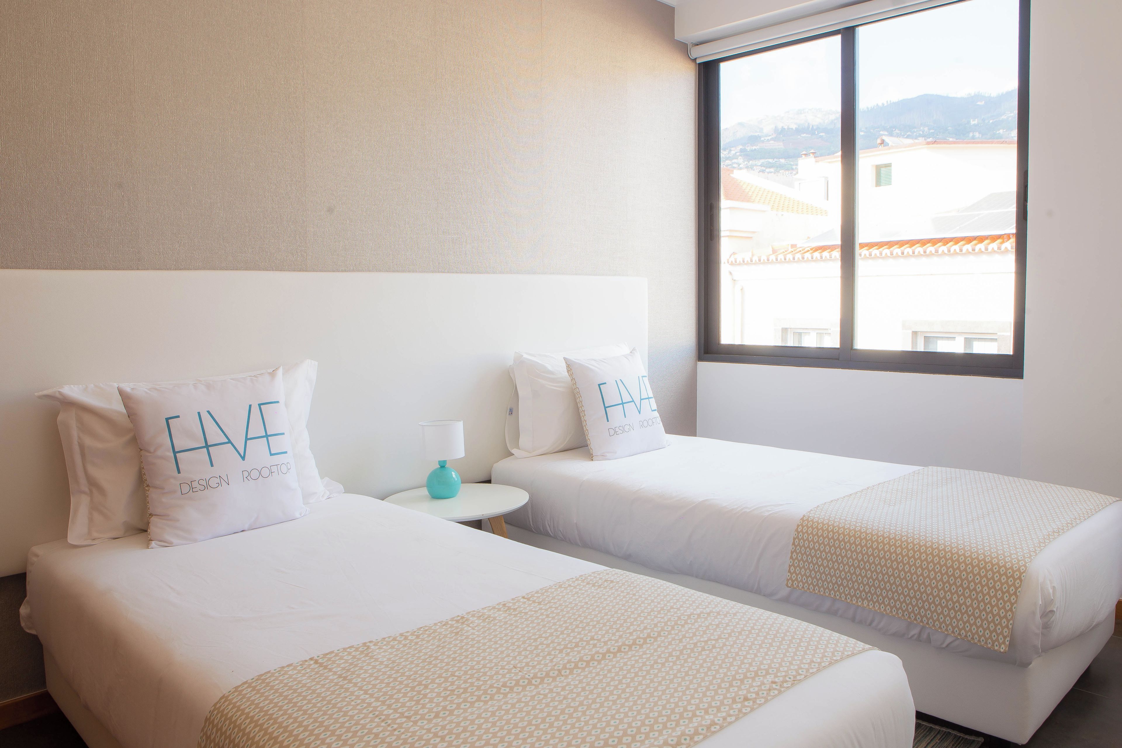 A hotel room with two beds, each with a pillow that reads "HAVE DESIGN ROOFING."