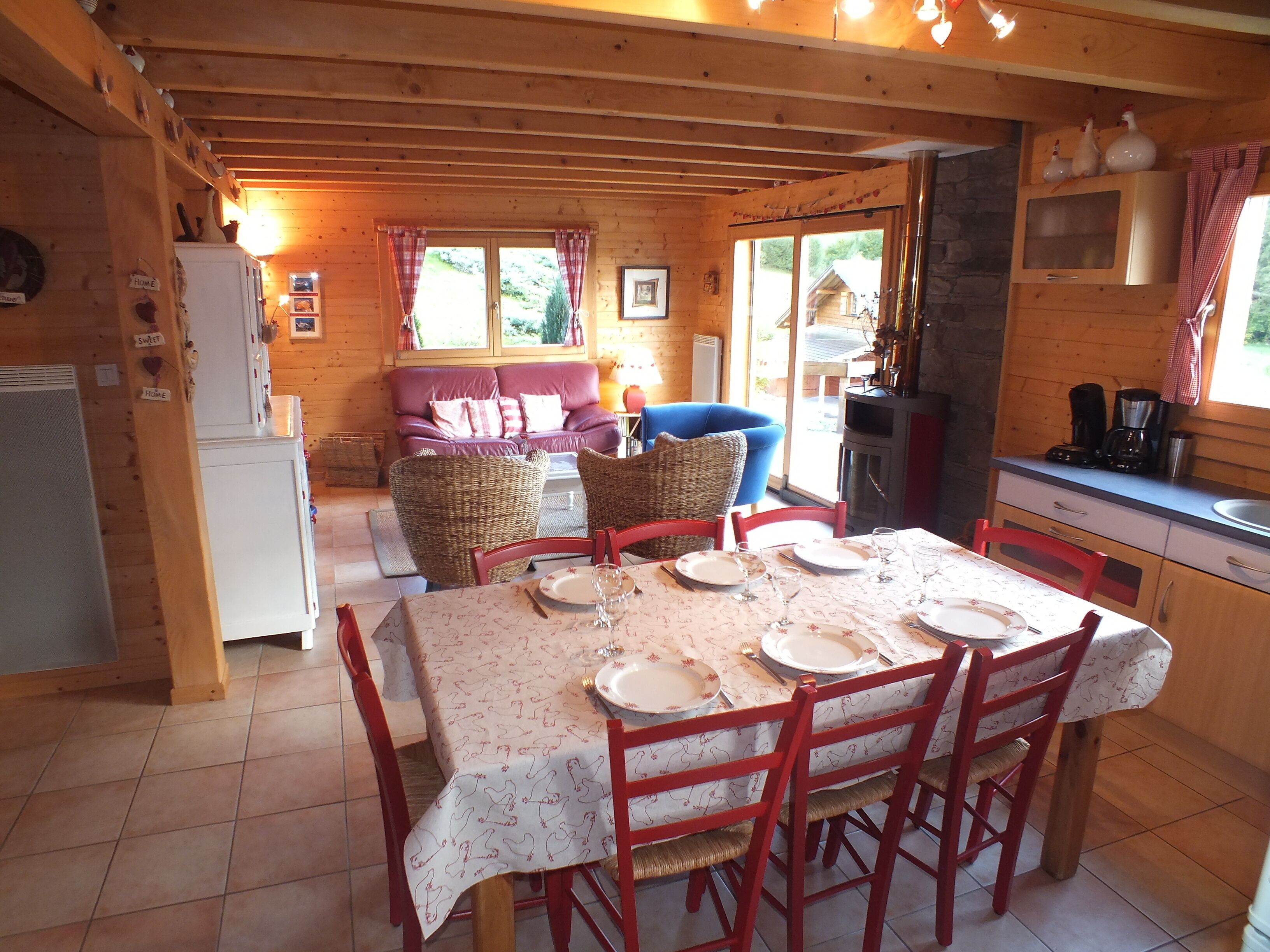 Une chaleureuse cabane en bois dotée d’un coin repas avec une table dressée pour quatre personnes, d’un canapé et d’un coin cuisine équipé d’une cuisinière et d’une machine à café.