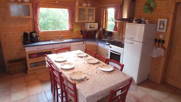 Une cuisine rustique aménagée dans une cabane en bois, avec une table à manger pour quatre personnes, un réfrigérateur, une cuisinière et un four à micro-ondes.