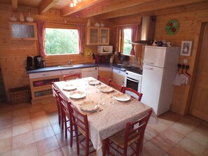 Een houten keukentje met een eettafel gedekt voor vier personen, een koelkast, een fornuis en een magnetron.