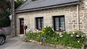 A stone house with a sloped roof, two windows with shutters, a small porch, and a flower bed with white flowers. -  Longére A Larmor-Plage, authentic charm of the stone. (Larmor-Plage)