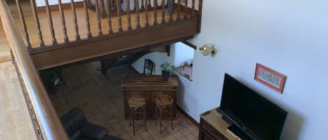 Una sala de estar con una escalera de madera, un televisor, una mesa de comedor con sillas y un sofá.