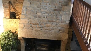 A stone fireplace with a wooden mantel, a potted plant, and a staircase with a wooden railing. -  Longére A Larmor-Plage, authentic charm of the stone. (Larmor-Plage)