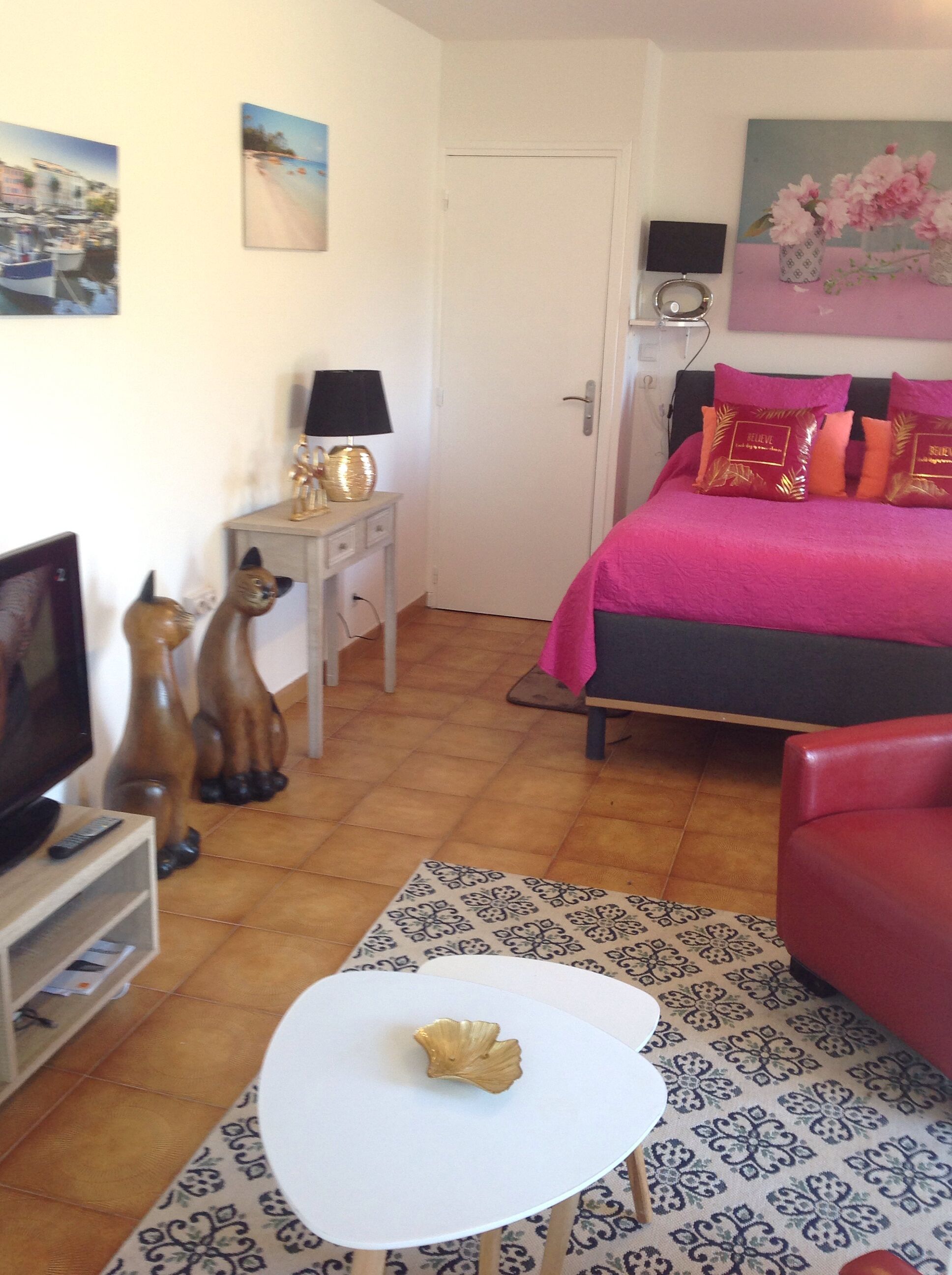Une chambre à coucher avec un lit, une télévision, une petite table, une porte et un mur orné d’un tableau.