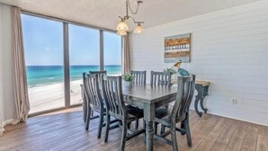 A dining area with a view of the beach, a wooden table, and chairs.
