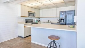 A modern kitchen with white cabinetry, a central island with a bar stool, a microwave, a refrigerator, and a coffee maker.
