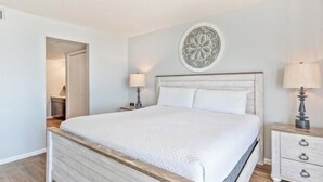 A bedroom with a wooden bed frame, white bedding, a decorative wall piece, and bedside lamps.