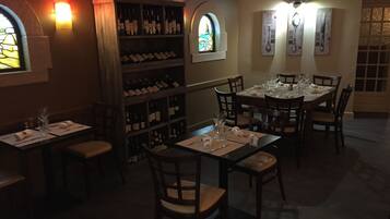 Un restaurante tenuemente iluminado con mesas y sillas de madera, bodegas y detalles decorativos en las paredes.
