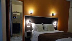 Una habitación de hotel con cama, mesita de noche y lámpara fijada a la pared.