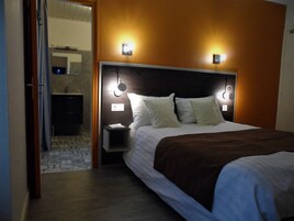 Quarto de hotel com cama, mesa de cabeceira e luminária fixada na parede.