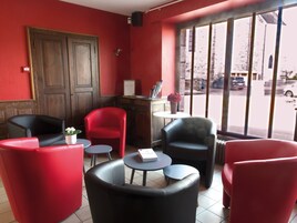 Uma área de estar com cadeiras vermelhas e pretas, uma pequena mesa e uma janela com vista para a rua.