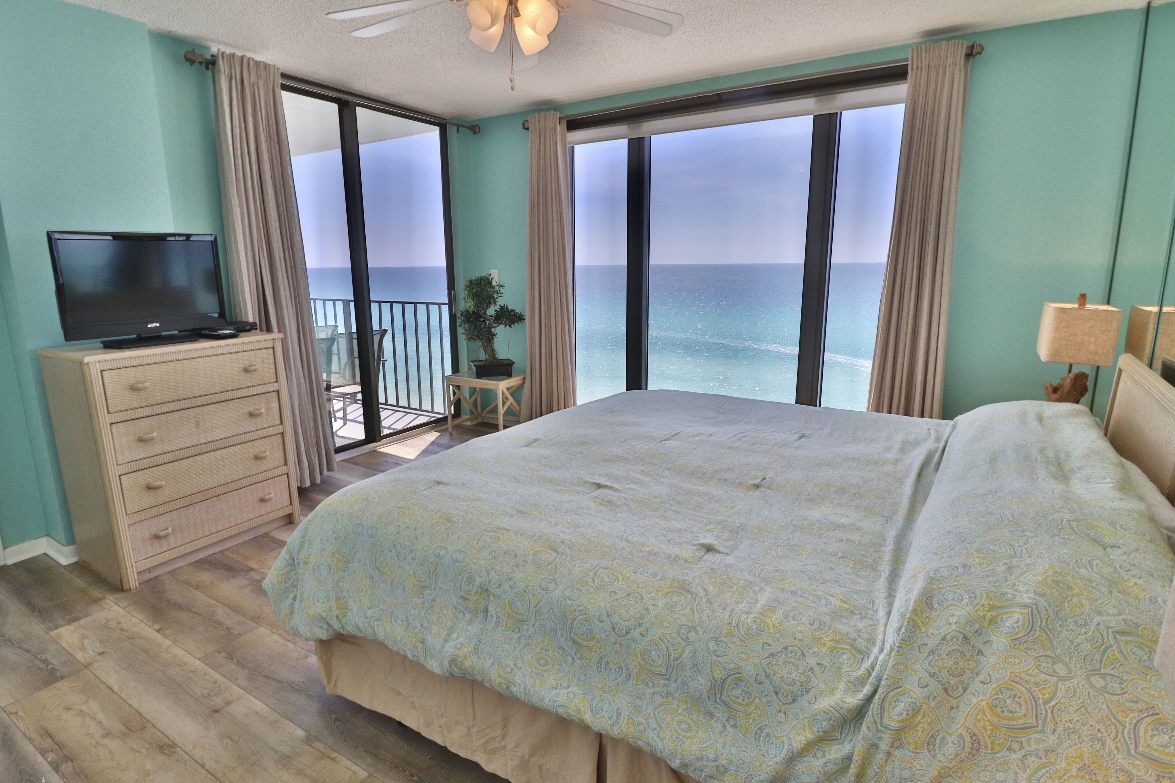 A bedroom with a large bed, a dresser, a television, and a view of the ocean.