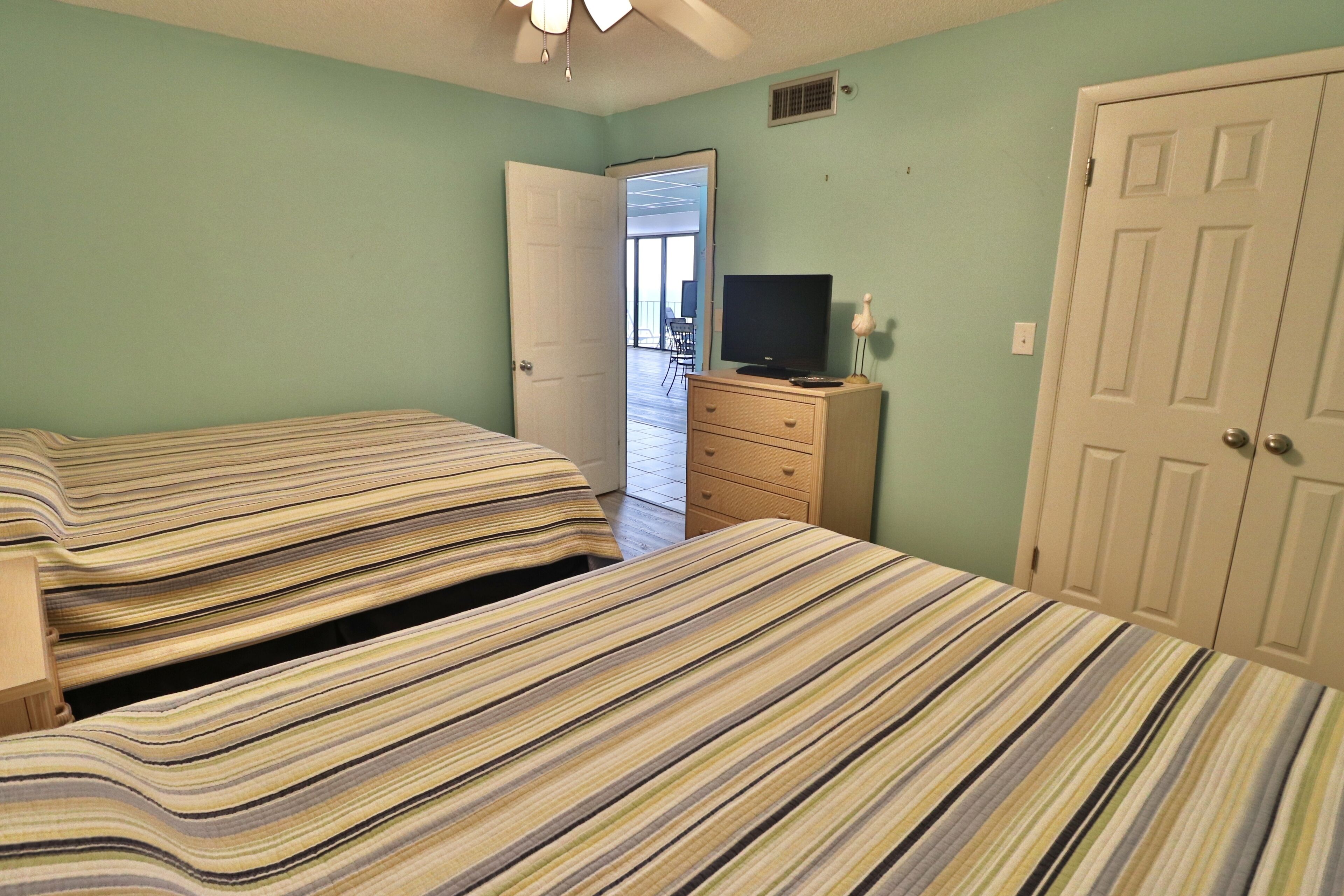 Une chambre avec deux lits, une commode, un téléviseur et une porte.