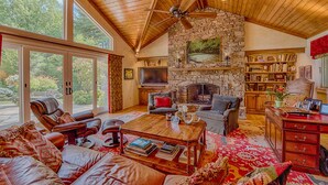 A spacious living room with leather sofas, a stone fireplace, and a large window overlooking a garden. - Luxury Home in Laurel Ridge Country Club Community (Waynesville)