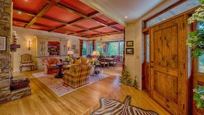 A spacious living room with a high ceiling, wooden beams, a fireplace, and a large wooden door. - Luxury Home in Laurel Ridge Country Club Community (Waynesville)