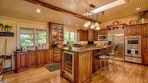 A spacious kitchen with wooden cabinets, a central island, bar stools, and stainless steel appliances. - Luxury Home in Laurel Ridge Country Club Community (Waynesville)