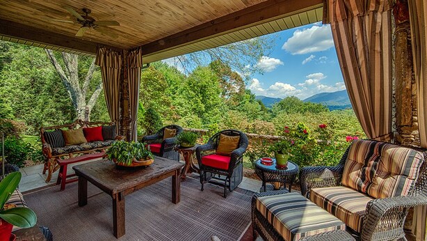 An outdoor patio with wicker furniture, a wooden table, and potted plants. - Luxury Home in Laurel Ridge Country Club Community (Waynesville)