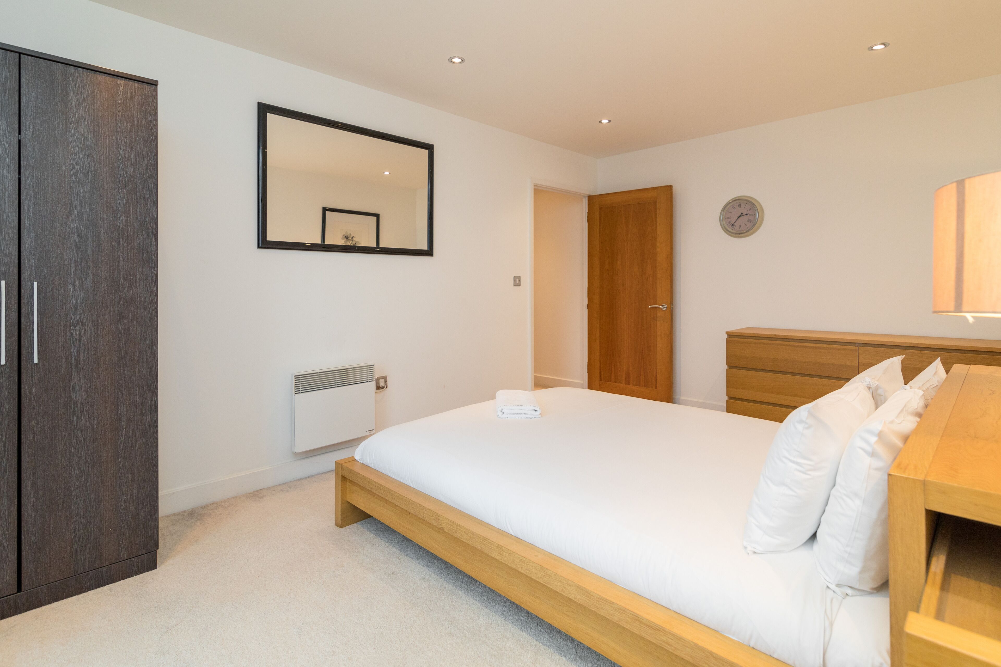 A bedroom with a bed, a wardrobe, a mirror, a clock, and a bedside table.