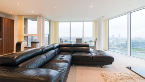 Uma sala de estar moderna com um sofá seccional de couro preto grande, uma mesa de centro de vidro e vista para a cidade através de amplas janelas.