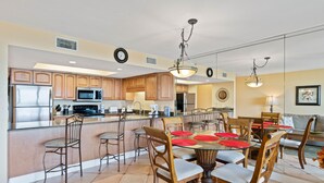 A spacious kitchen with wooden cabinets, a stainless steel refrigerator, and a microwave. There is a dining area with a round table, chairs, and red placemats.