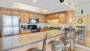 A kitchen with wooden cabinets, stainless steel appliances, a granite countertop, and bar stools.