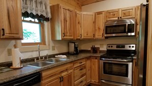 A kitchen with wooden cabinets, a stainless steel refrigerator, a microwave, and an oven. - RIVERFRONT ADIRONDACK LOG CABIN (Warrensburg)