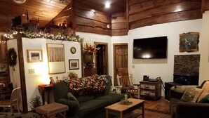 A cozy living room with wooden floors, a green sofa, a coffee table, and a fireplace. - RIVERFRONT ADIRONDACK LOG CABIN (Warrensburg)