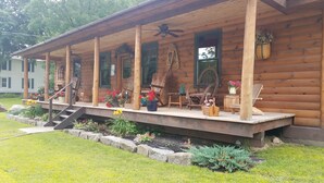 A log cabin with a porch, outdoor seating, and a staircase leading to the entrance. - RIVERFRONT ADIRONDACK LOG CABIN (Warrensburg)
