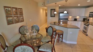 A dining area with a glass table and chairs, a kitchen with white cabinets, and a small island with a refrigerator and microwave.