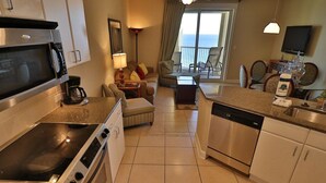 A modern kitchen with a stove, microwave, and dishwasher. There is a dining area with a table and chairs, and a view of the ocean through large windows.