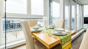 A dining area with a table set for four, large windows, and a view of the cityscape. - Grand Vista by Austin David Apartments (London)