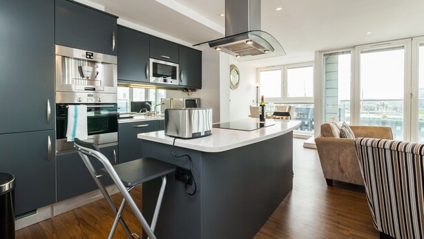 A modern kitchen with stainless steel appliances, a central island, and a view of the city through large windows. - Grand Vista by Austin David Apartments (London)