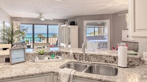 A kitchen with granite countertops, a double sink, and a view of the ocean.